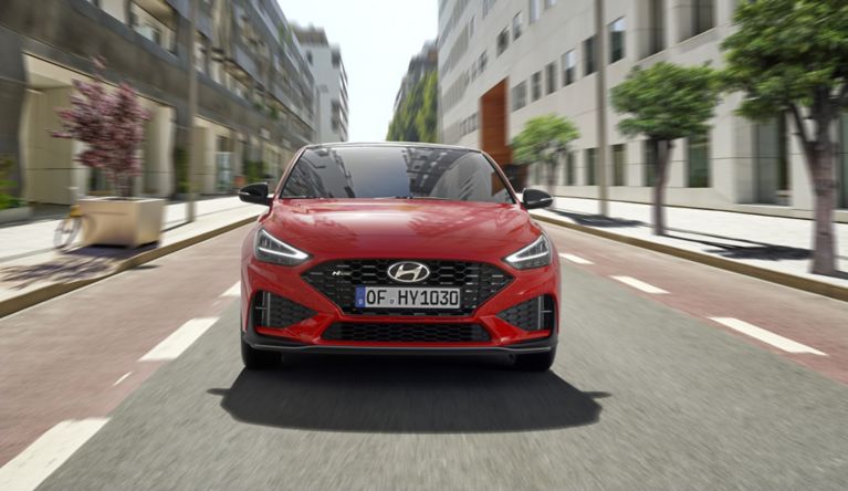 A red car driving down a street

Description automatically generated